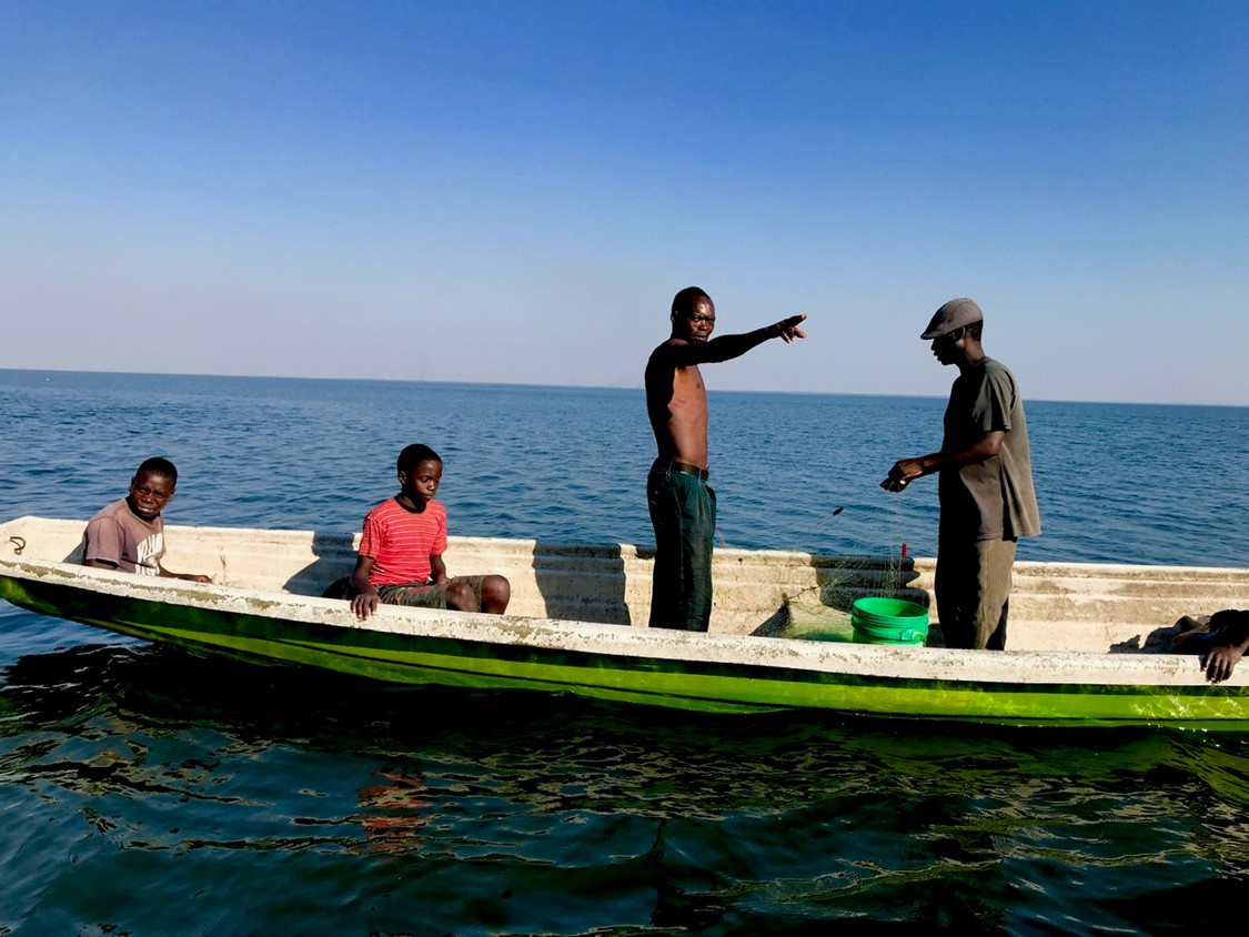 A man points across the water from a small boat, accompanied by another man and two young boys.